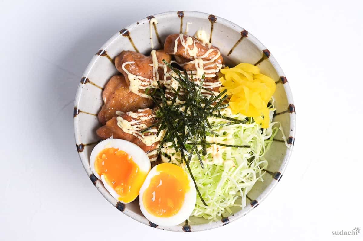 Garlic teriyaki chicken donburi with shredded cabbage, soft boiled eggs, takuan (yellow pickled daikon), mayo and kizami nori on top.