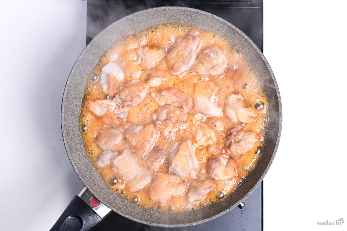 seared chicken thigh pieces in a frying pan in bubbling teriyaki sauce