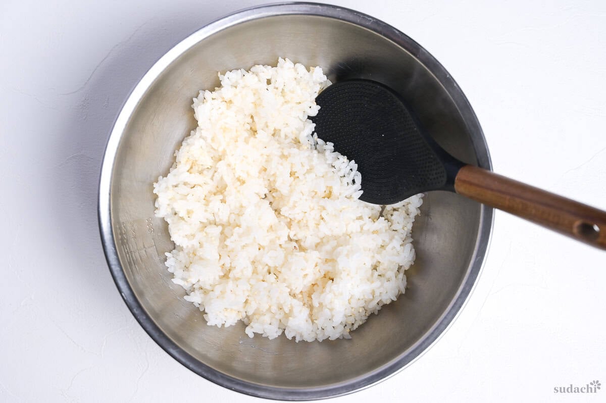white Japanese rice mixed with sesame seeds in a steel mixing bowl with rice paddle.