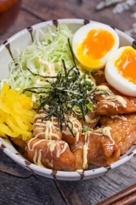 Garlic teriyaki chicken donburi with shredded cabbage, soft boiled eggs, takuan pickles and nori served in a striped bowl