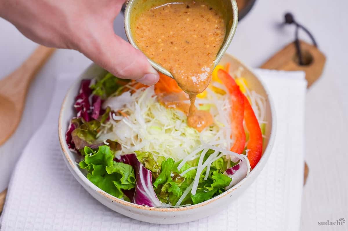 Pouring homemade Japanese goma sesame dressing over mixed salad bowl