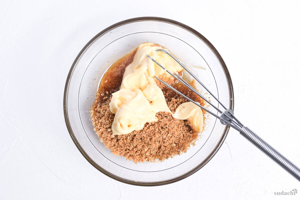 Adding Japanese mayonnaise and toasted ground white sesame seeds to goma dressing ingredients in a glass bowl