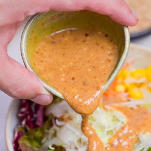 Pouring homemade Japanese goma sesame dressing over salad.