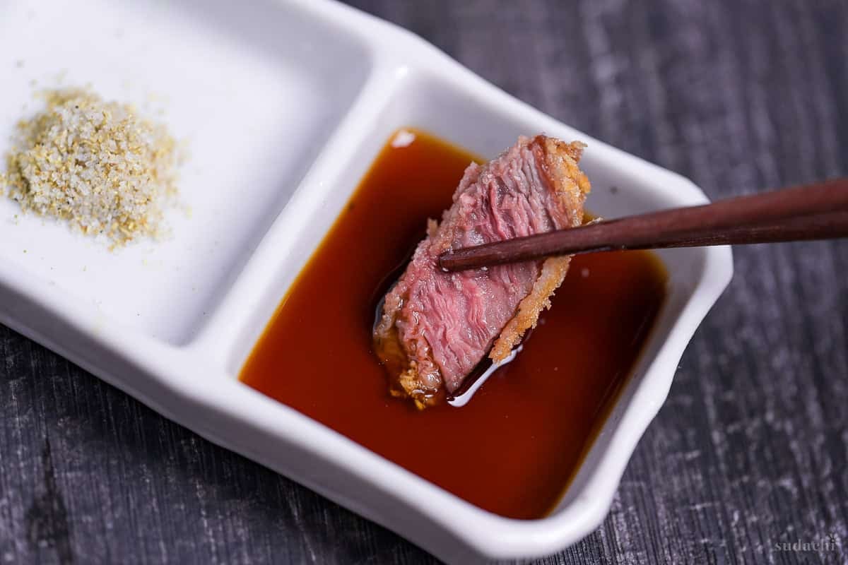 a close up of gyukatsu being dipped in homemade sauce
