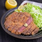 Gyukatsu (Japanese beef cutlet) cooked rare and served on a wire rack with shredded cabbage, lemon slices and wasabi with dipping sauces behind