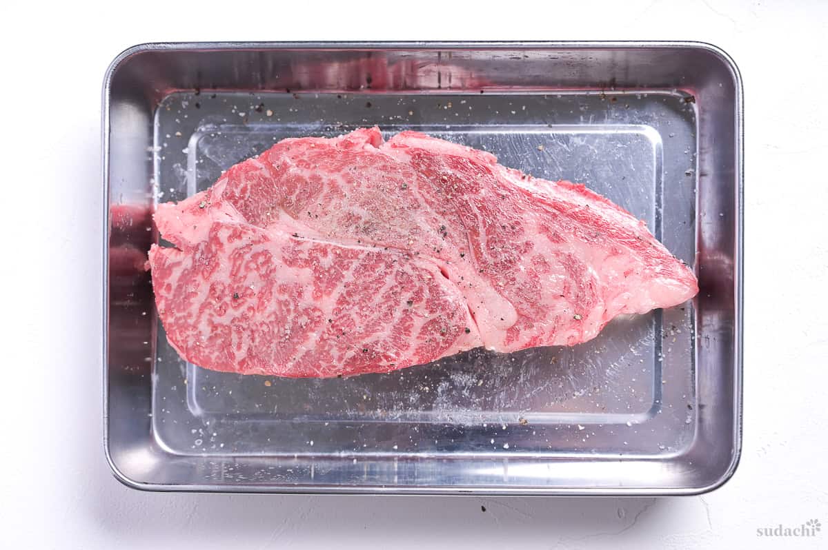 beef steak seasoned with salt and pepper in a steel container