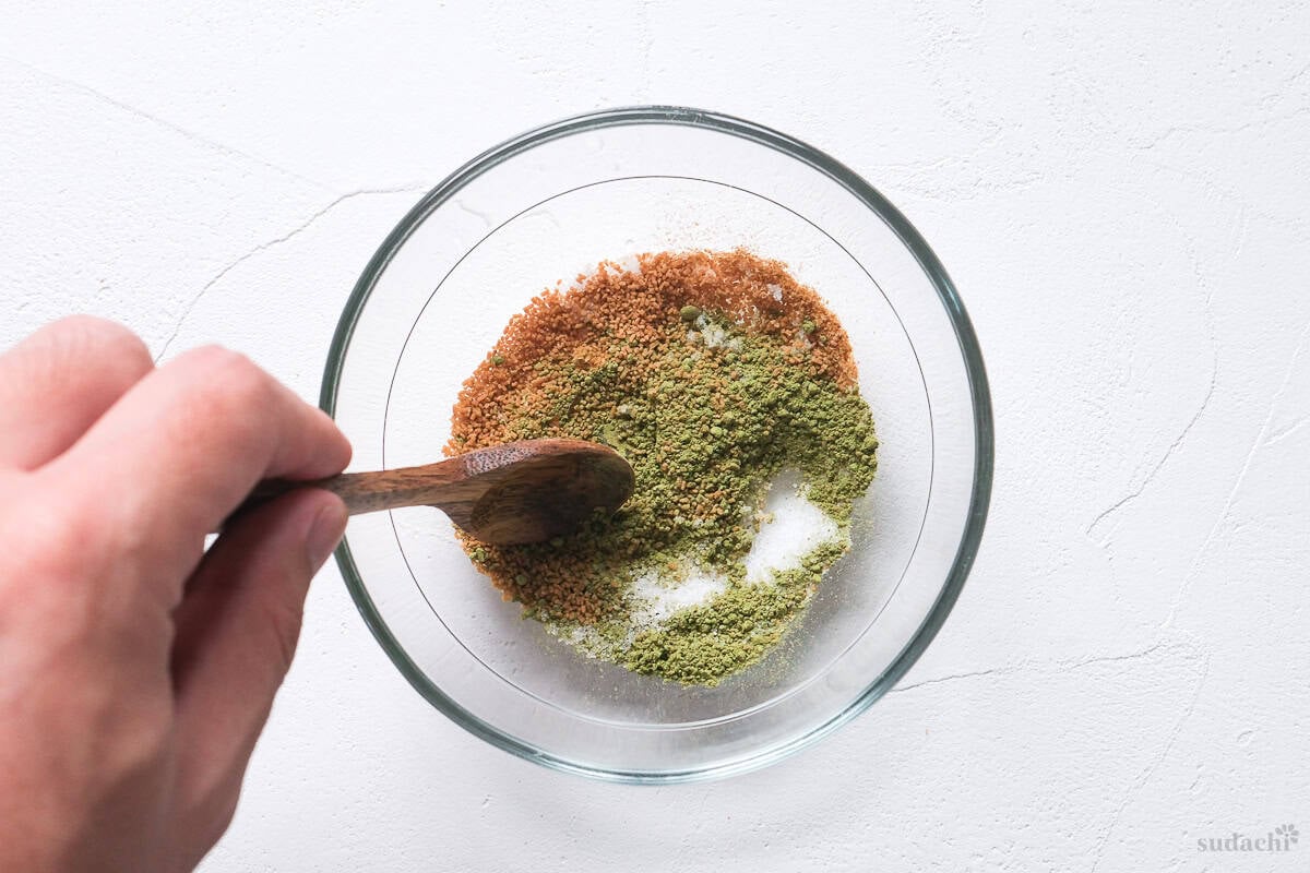 homemade instant ochazuke ingredients with matcha in a glass bowl being mixed with a wooden spoon