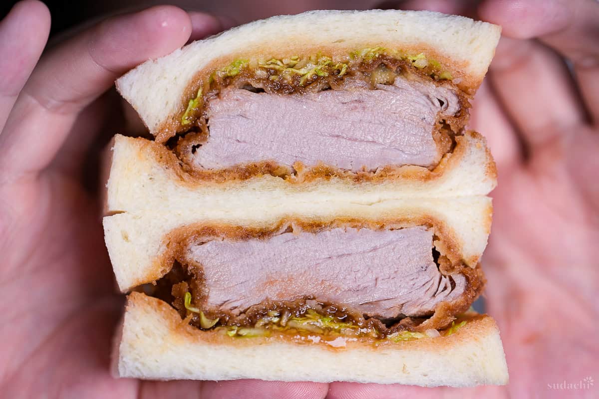 Yuto Omura holding up a katsu sando (Japanese pork cutlet sandwich) cut in half to reveal cross section