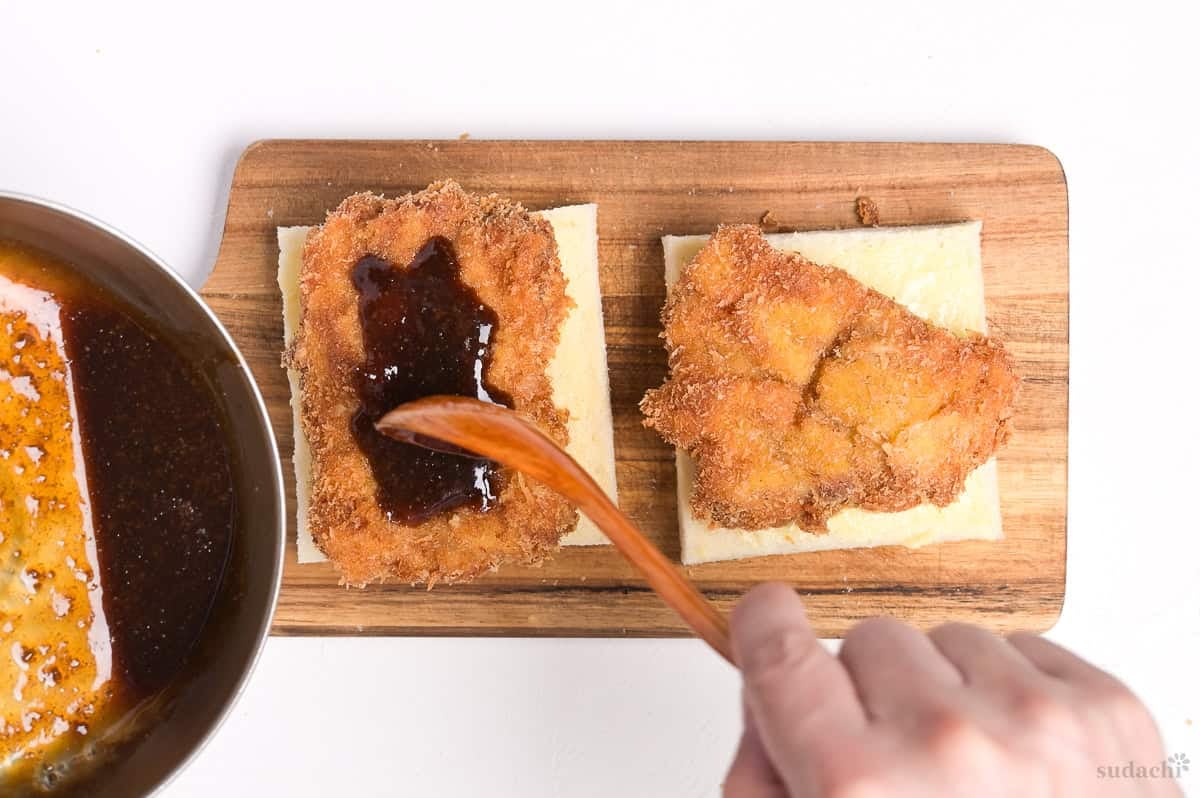 spooning homemade katsu sauce over pork cutlets to make katsu sando