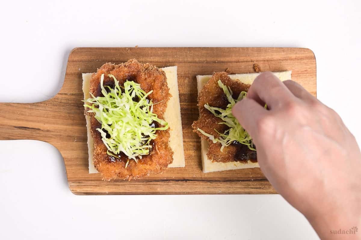 Placing shredded cabbage on top of pork cutlets to make katsu sando