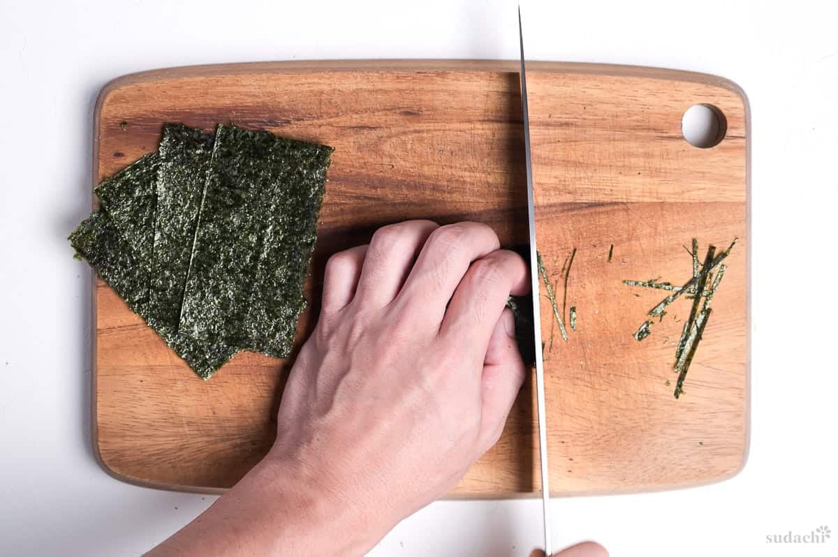 cutting kizami nori with a knife on a wooden cutting board