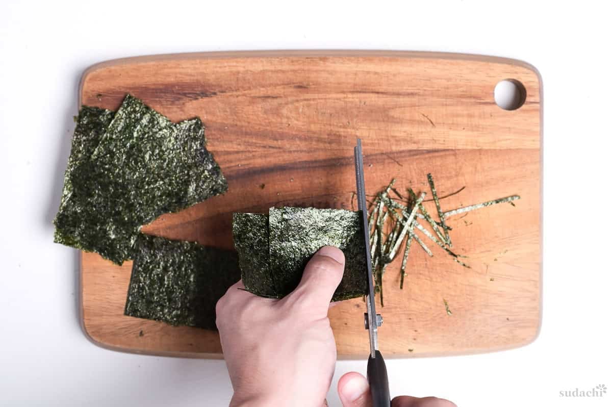 cutting kizami nori with scissors on a wooden cutting board