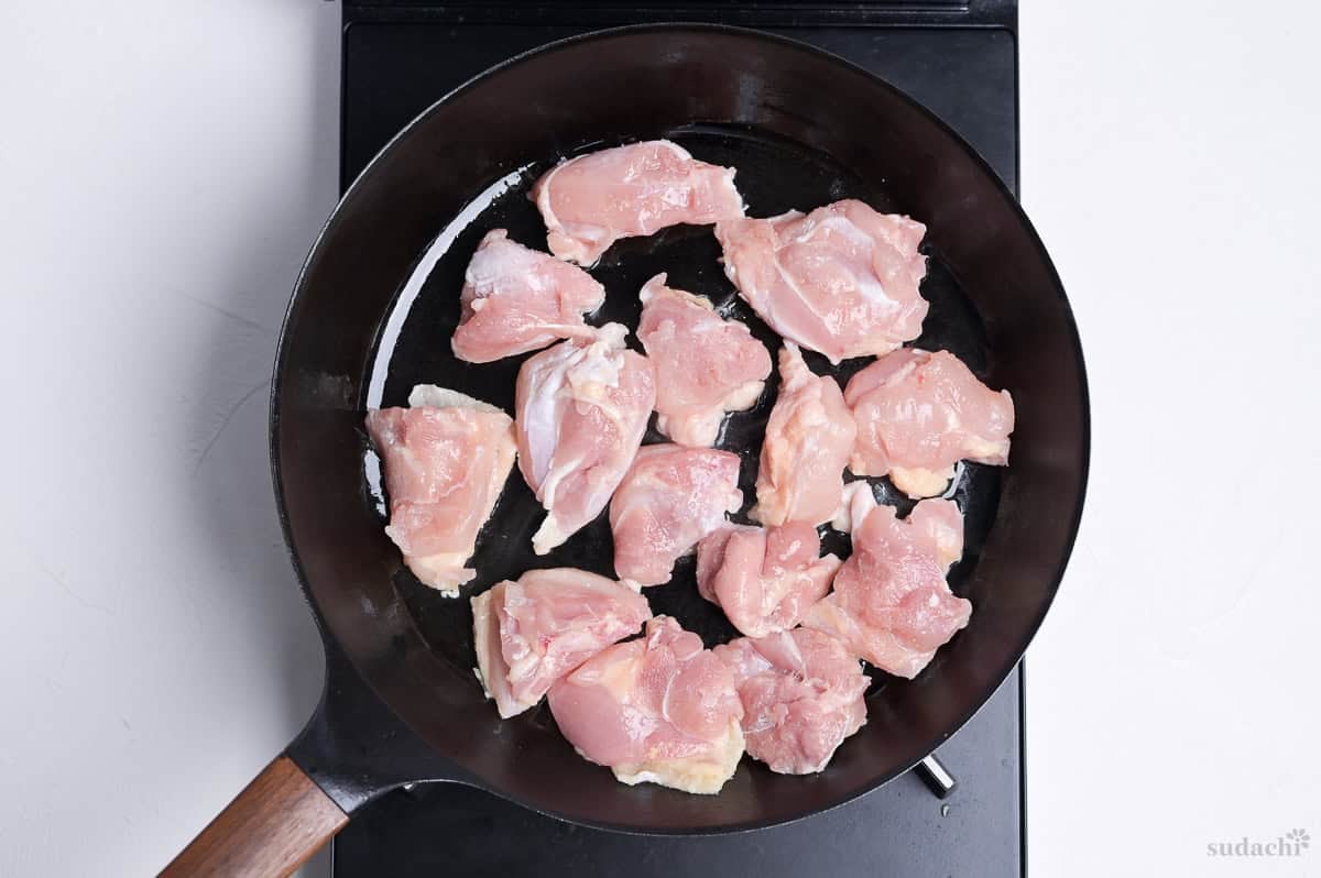 Pieces of chicken thigh frying in a pan with the skin side facing down