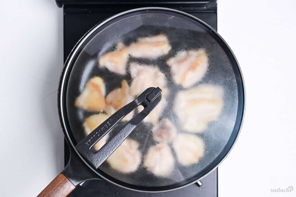 pieces of chicken thigh frying in a pan with lid on top