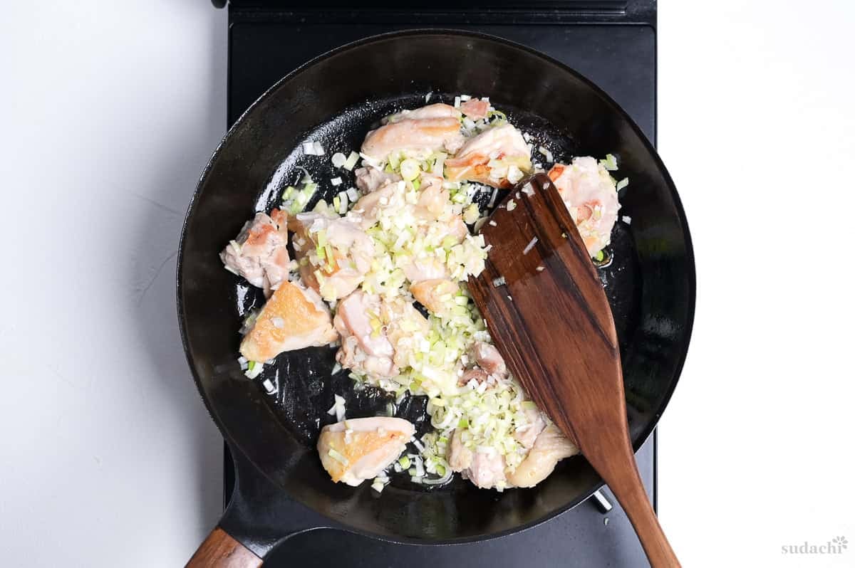 seared chicken thigh in a pan with finely chopped Japanese leek and garlic