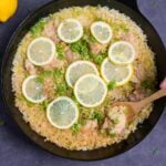 Japanese style negi shio paella with chicken and lemon in a black frying pan topped with lemon slices and finely chopped green onion with wooden spoon scooping (top down)