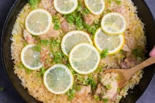 Japanese style negi shio paella with chicken and lemon in a black frying pan topped with lemon slices and finely chopped green onion with wooden spoon scooping (top down)