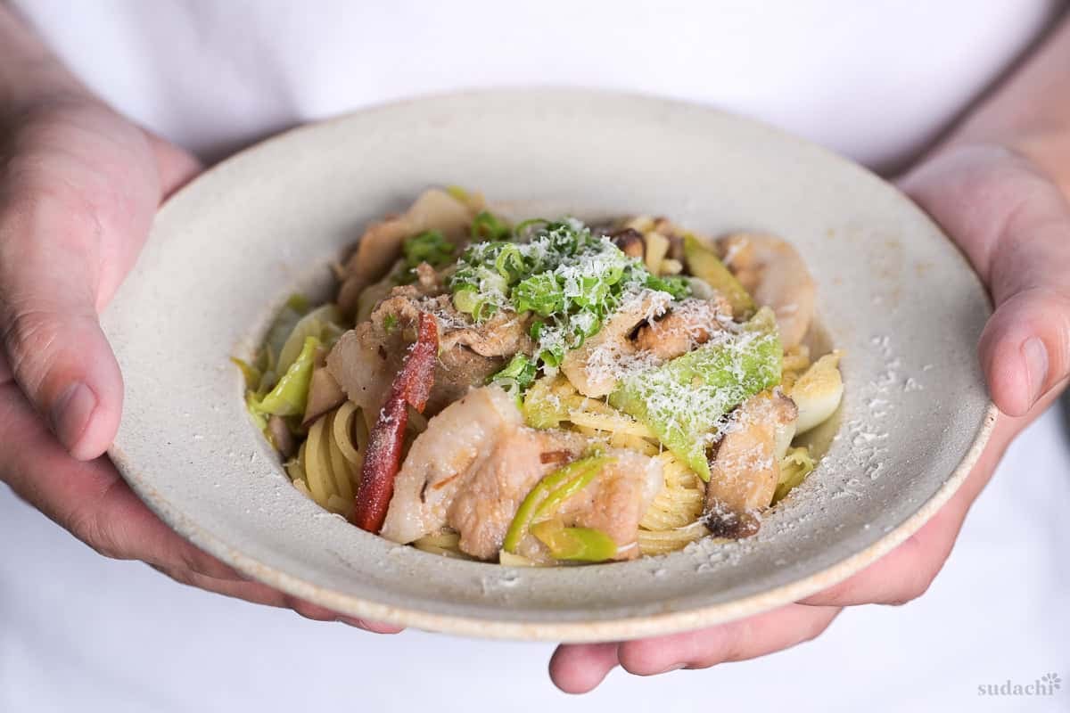 Yuto Omura holding up a plate of negishio spaghetti topped with chopped green onions and shredded parmesan cheese
