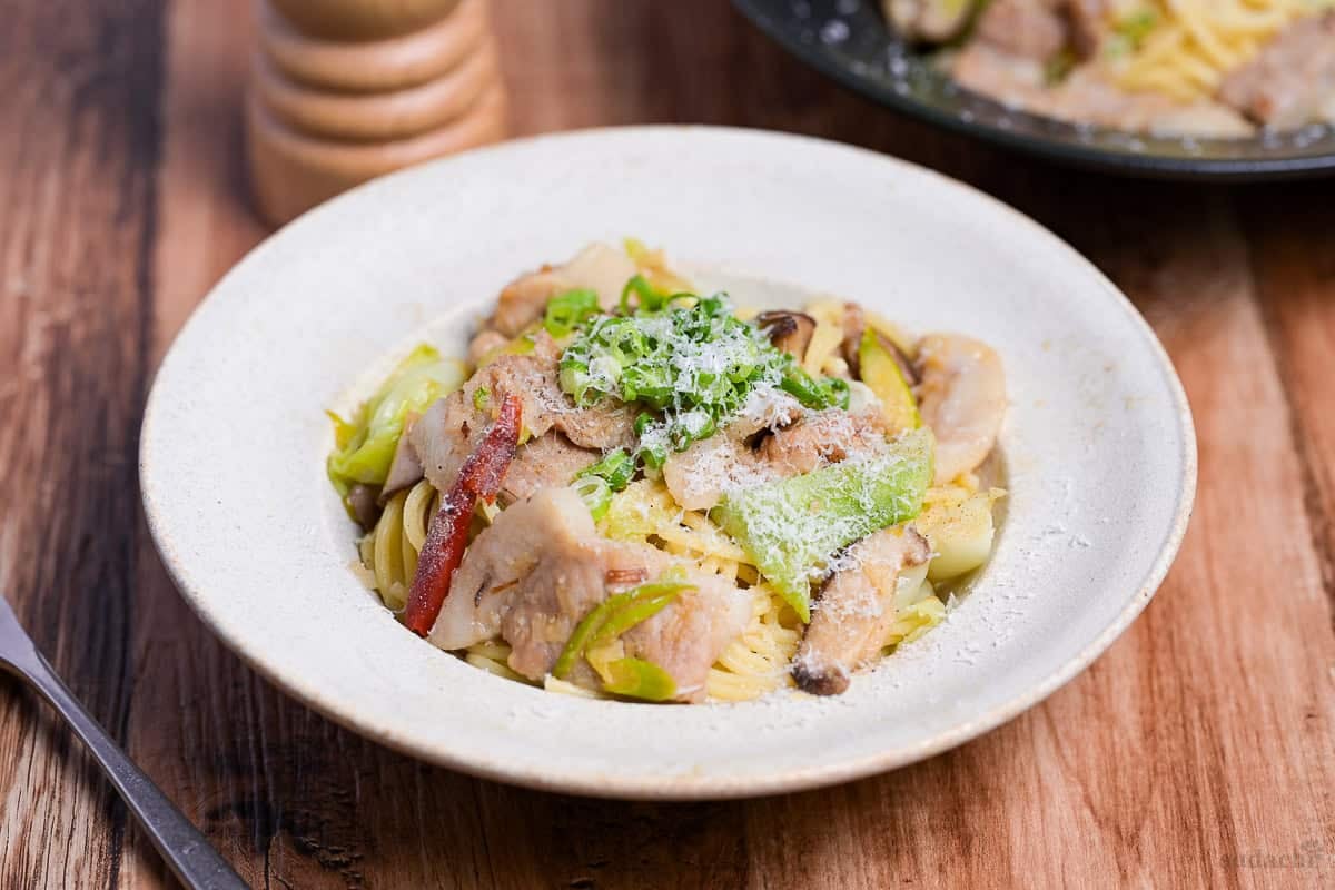 Negishio spaghetti topped with chopped green onions and shredded parmesan cheese in an off-white pasta dish. side view