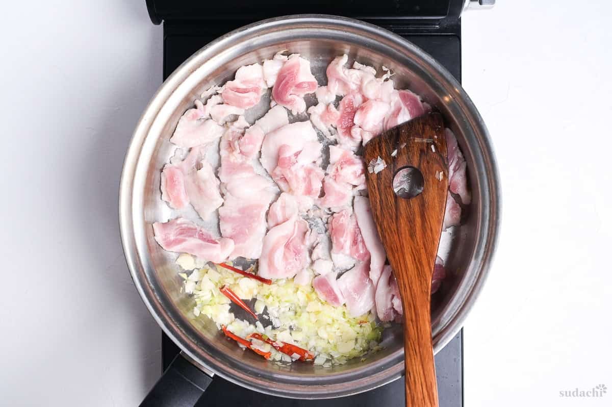 searing thinly sliced pork belly in a frying pan on the stove top