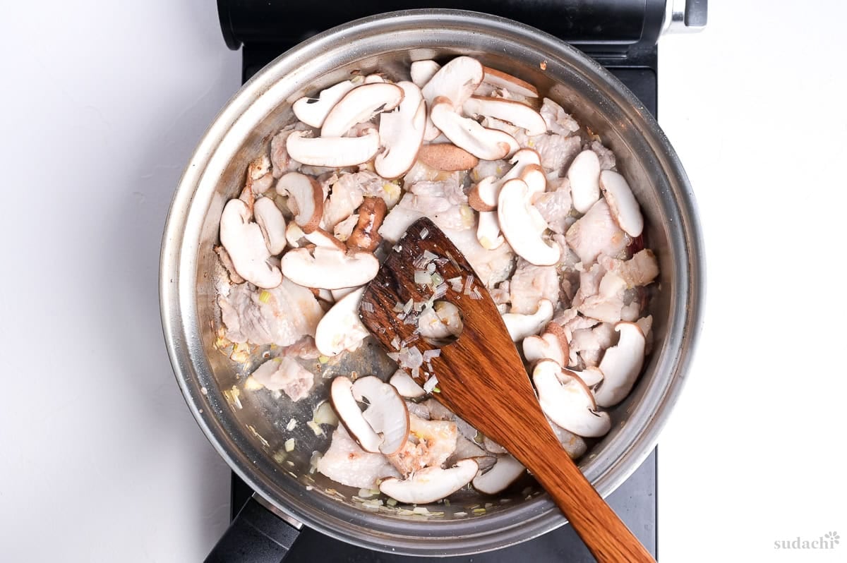 frying aromatics, pork belly and shiitake mushrooms in a large pan on the stovetop