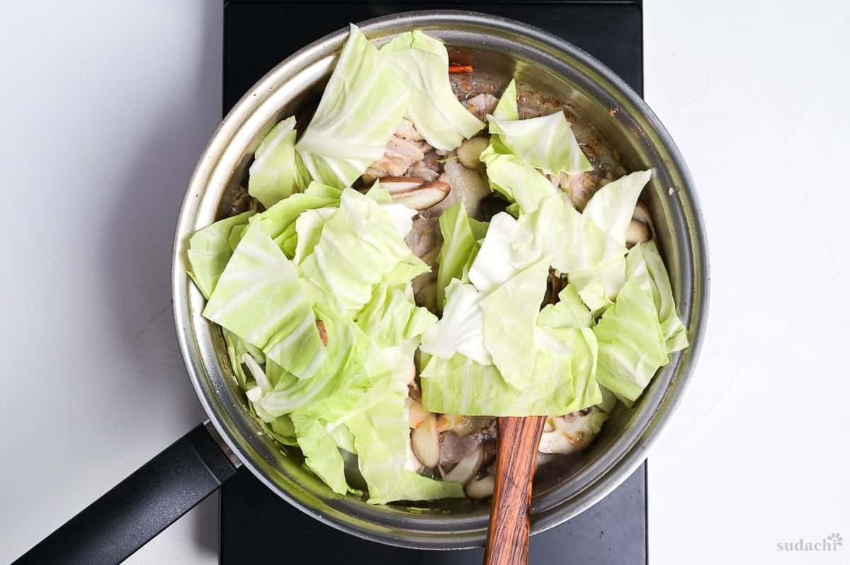 adding roughly cut green cabbage to a large pan to make negishio spaghetti