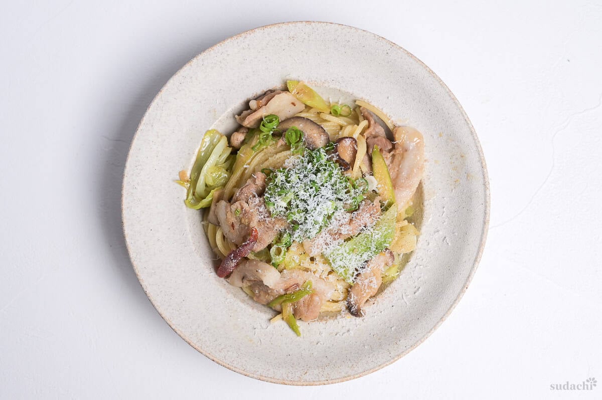 Negishio spaghetti with thinly sliced pork belly topped with chopped green onions and shredded parmesan cheese in an off-white pasta dish