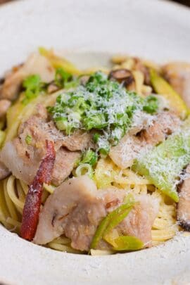 Negishio spaghetti topped with chopped green onions and shredded parmesan cheese in an off-white pasta dish. thumbnail close up