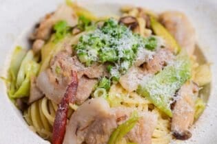 Negishio spaghetti topped with chopped green onions and shredded parmesan cheese in an off-white pasta dish. thumbnail close up