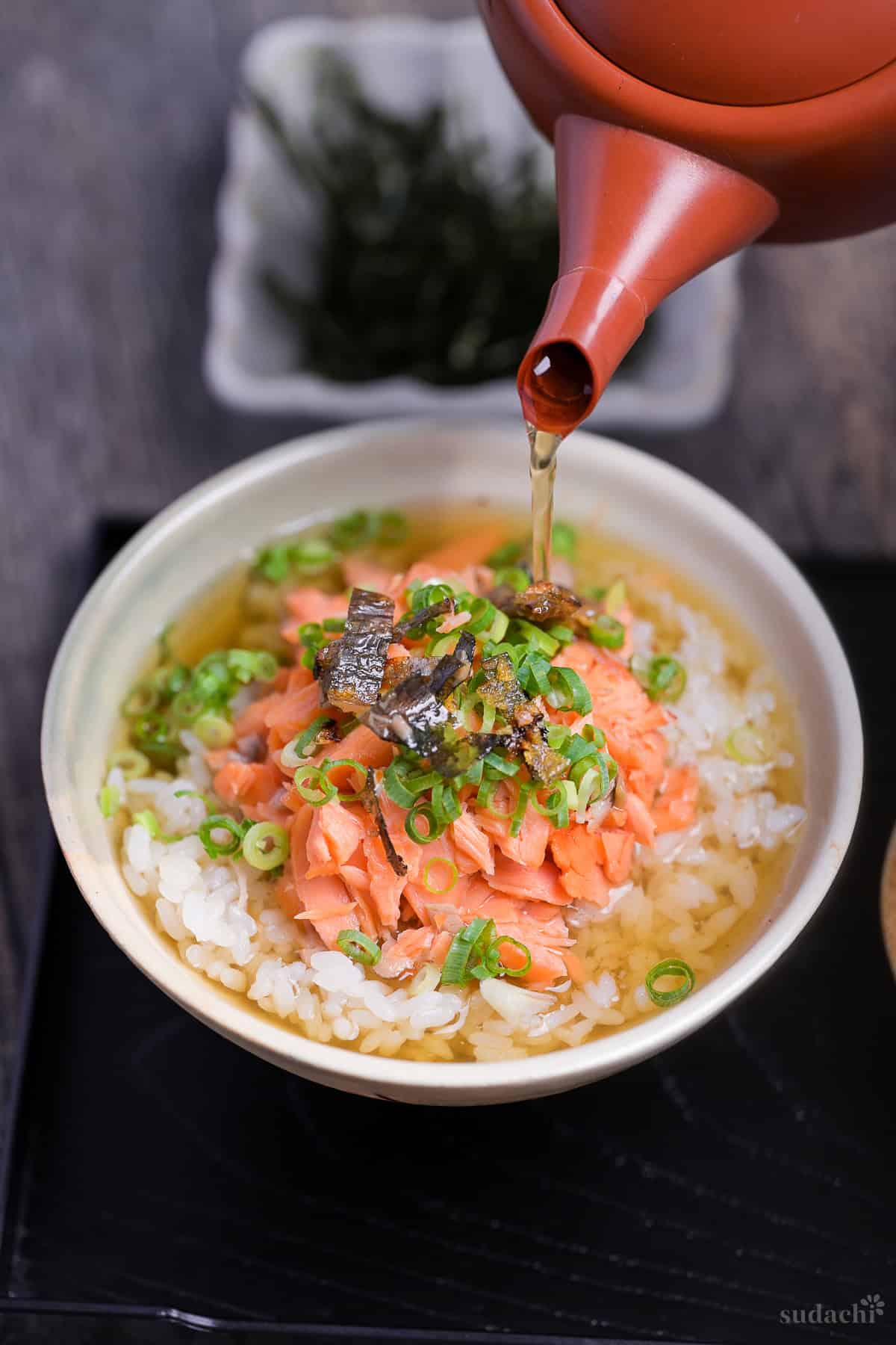 dashi green tea poured over rice and salmon in a cream ceramic bowl to make ochazuke