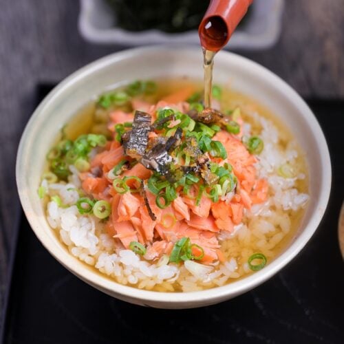 dashi green tea poured over rice and salmon in a cream ceramic bowl to make ochazuke