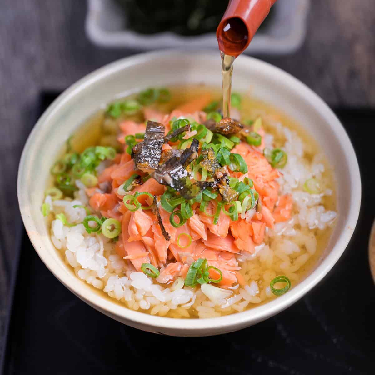dashi green tea poured over rice and salmon in a cream ceramic bowl to make ochazuke
