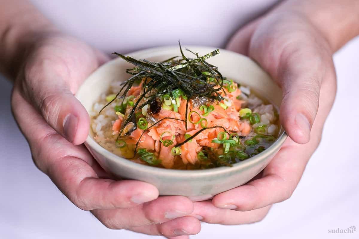 Yuto Omura holding up a bowl of ochazuke topped with salmon flakes, chopped green onions and shredded kizami nori.