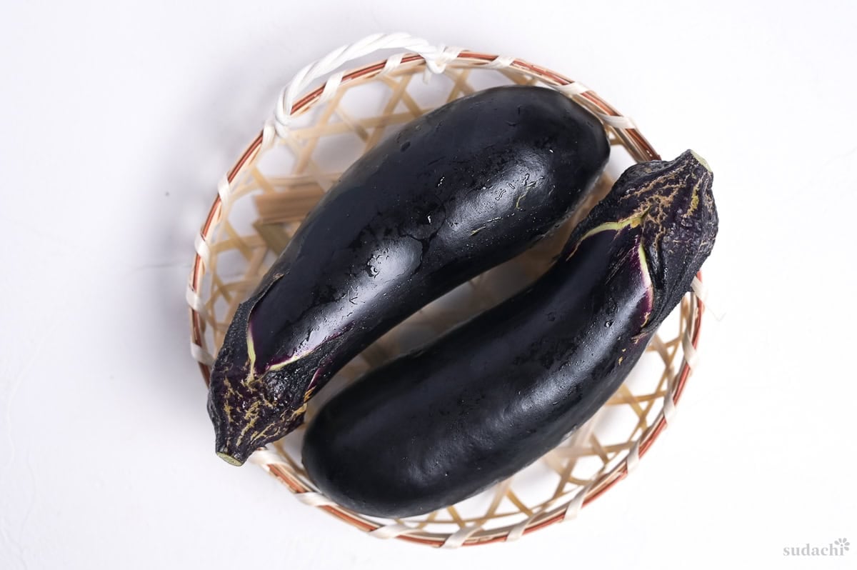 two Japanese eggplants in a small woven basket on a white background