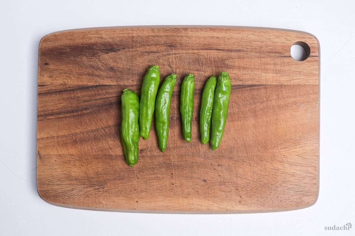 six shishito peppers on a wooden cutting board