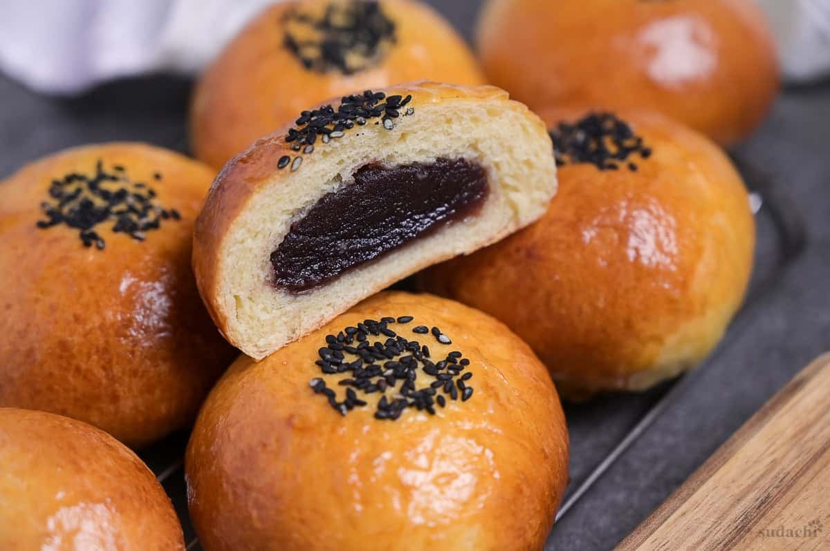 homemade anpan (Japanese red bean bun) cut in half to reveal anko in the center placed on top of whole buns