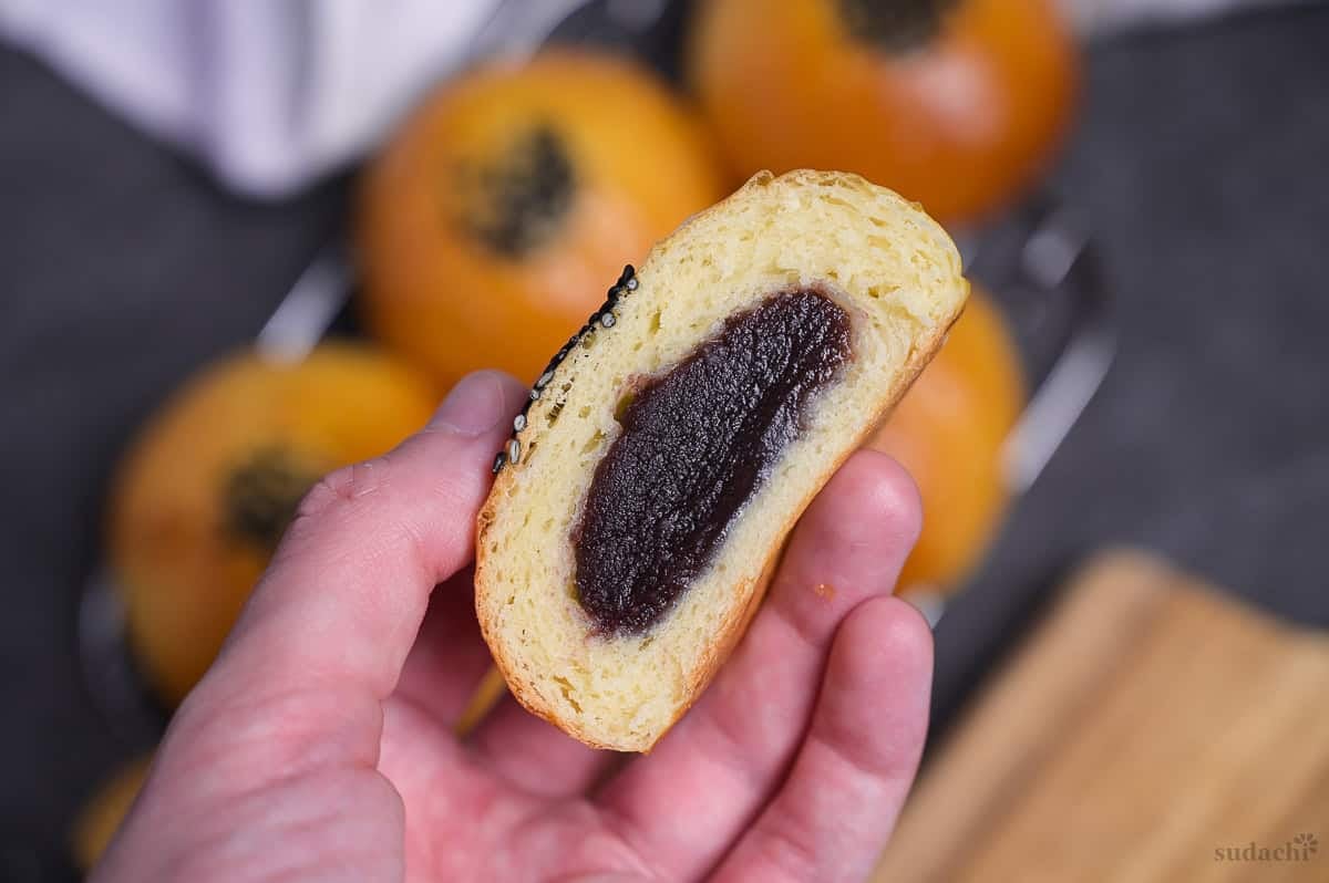A hand holding up homemade anpan (Japanese red bean bun) cut in half to reveal anko in the center