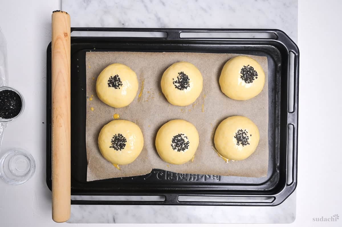 anpan with egg wash and black sesame seeds on a baking tray ready to go into the oven