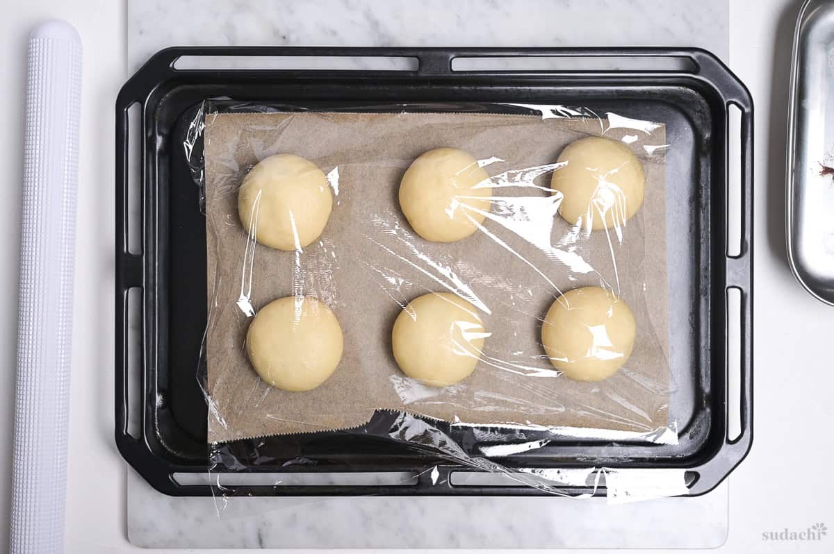 6 anpan on a baking sheet covered with plastic wrap for second rise