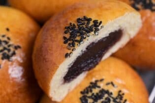 A homemade anpan Japanese red bean bun topped with black sesame seeds and cut in half to reveal anko filling in the center.
