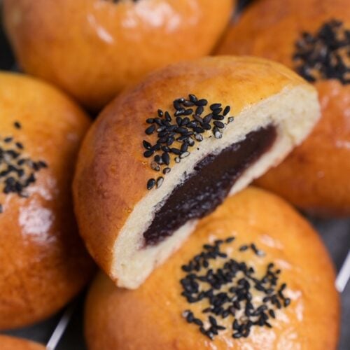 A homemade anpan Japanese red bean bun topped with black sesame seeds and cut in half to reveal anko filling in the center.