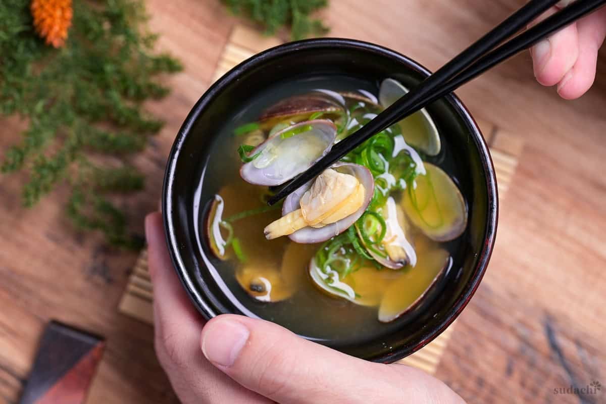black chopsticks lifting open clam out of miso soup top down view