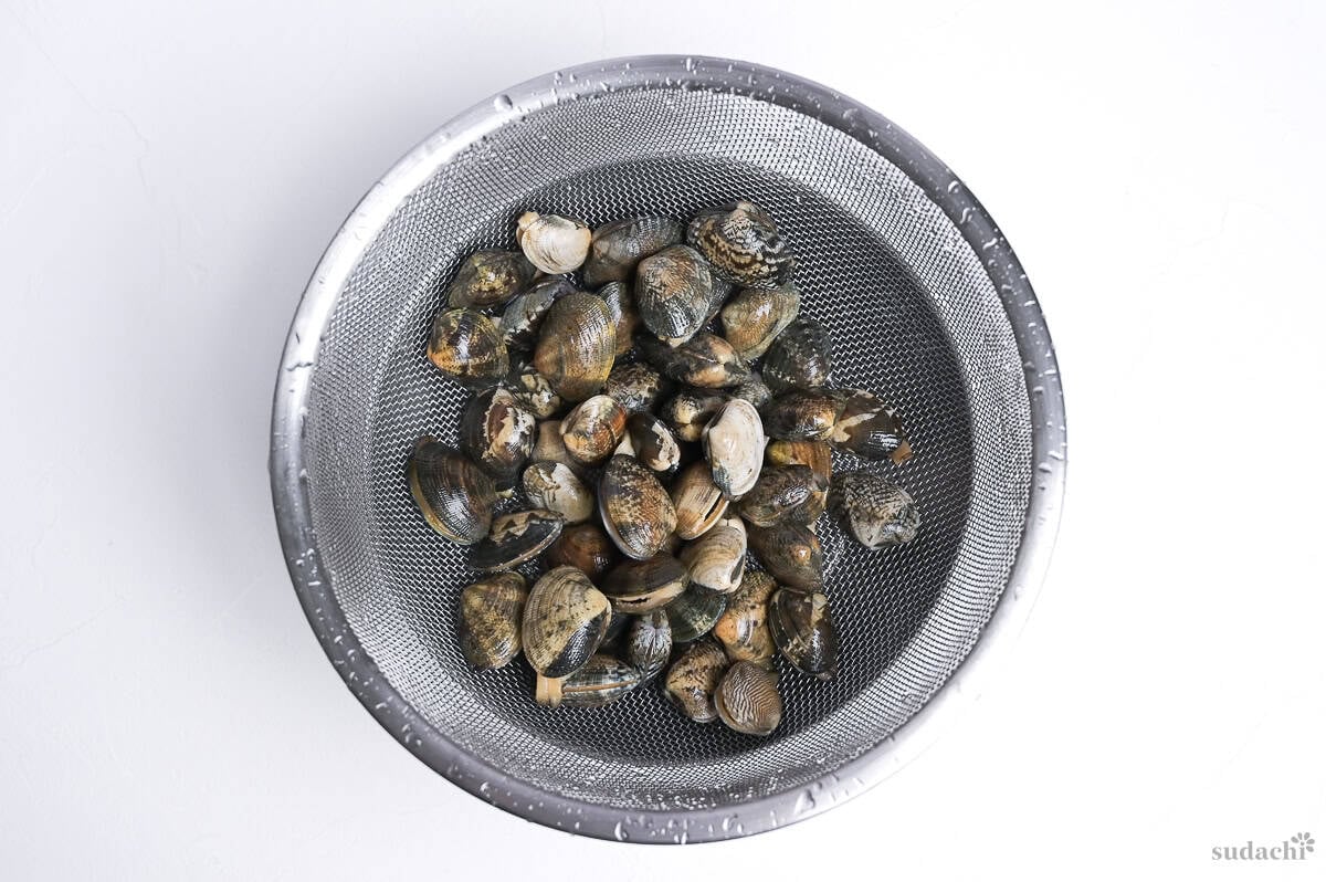 Fresh manila clams in a steel sieve over a mixing bowl