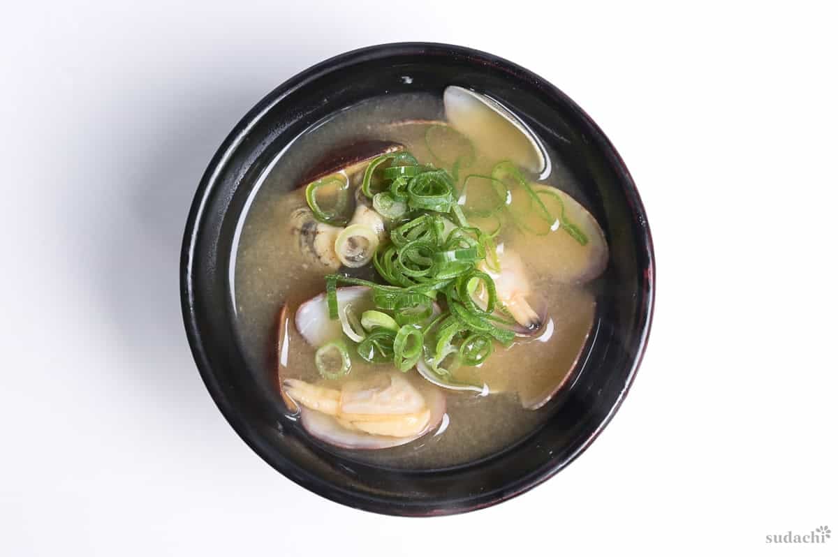 Asari miso soup topped with chopped green onions in a black bowl on a white background