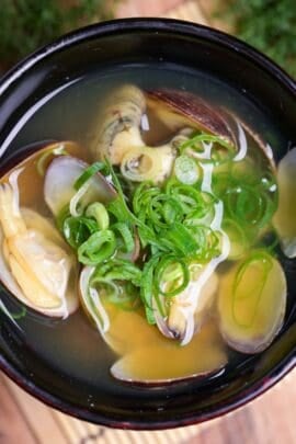 Homemade asari (clam) miso soup topped with green onions served in a small black Japanese soup bowl
