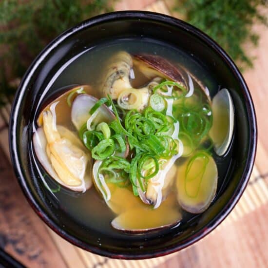 Homemade asari (clam) miso soup topped with green onions served in a small black Japanese soup bowl