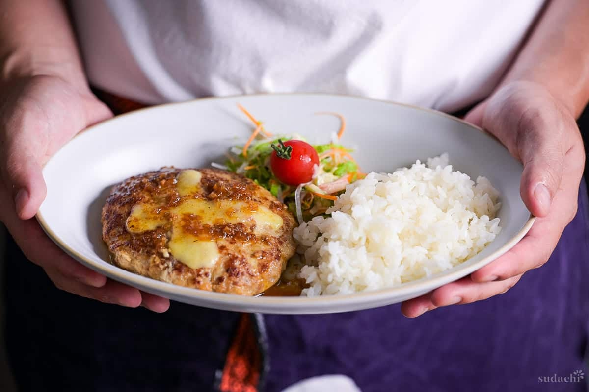 Yuto Omura holding Bikkuri Donkey copycat hamburg (burg) on a oval plate with rice and salad