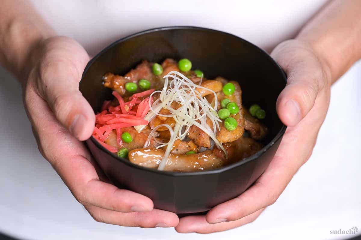 Yuto Omura holding a bowl of butadon topped with green peas, pink pickled ginger (benishoga) and shredded negi (shiraganegi)