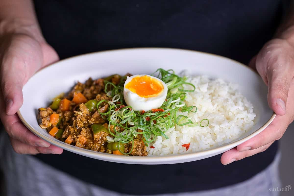 Yuto Omura holding Japanese style dry curry with rice and soft boiled egg on a white oval plate