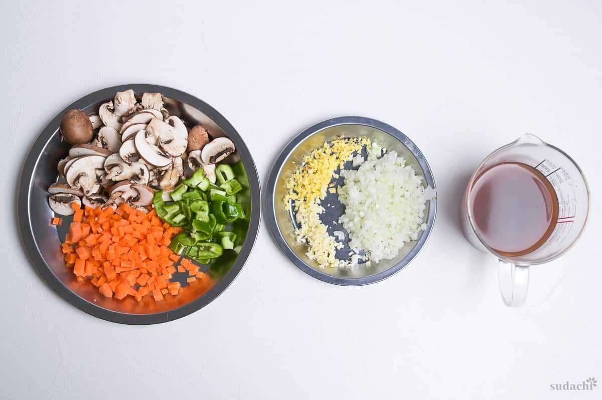 Ingredient prep for dry curry: sliced button mushrooms, diced carrot, diced bell peppers, finely diced ginger, garlic and onion, and sauce mixed in a glass measuring jug.